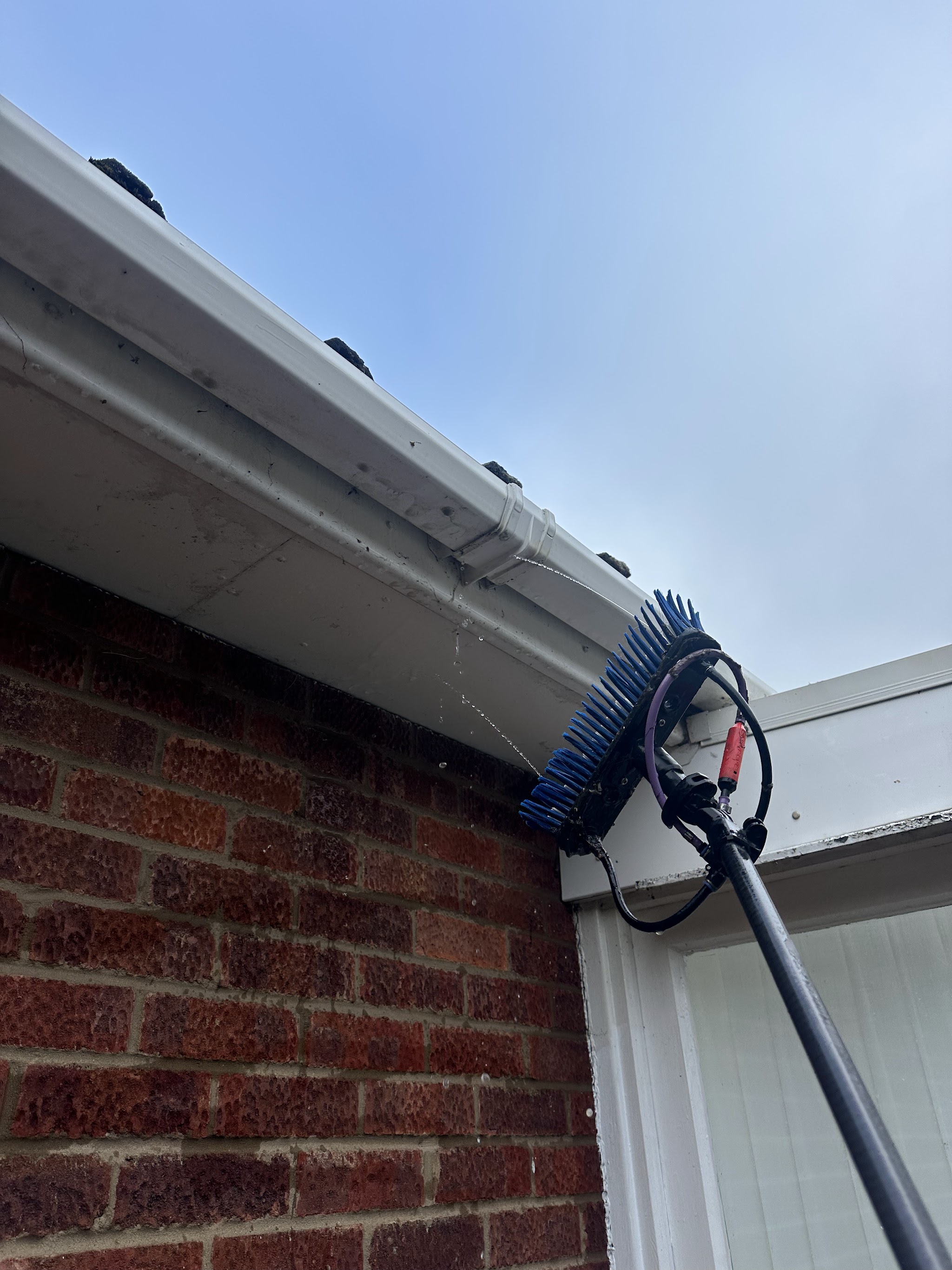 A gutter brush on a pole cleaning white fascia and guttering